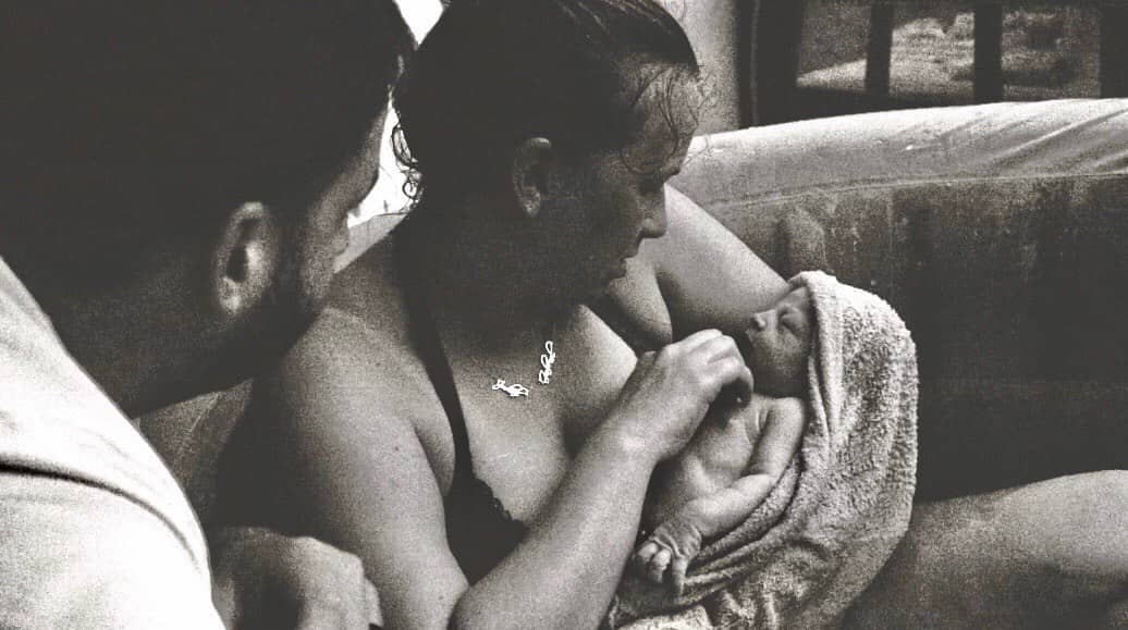 A family moment during a water birth at home in Indiana, supported by a licensed midwife, with the newborn being held close by the mother.